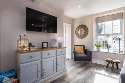 a living room with a dresser with a television on the wall at Seagrass Cottage - Aberdovey in Aberdyfi