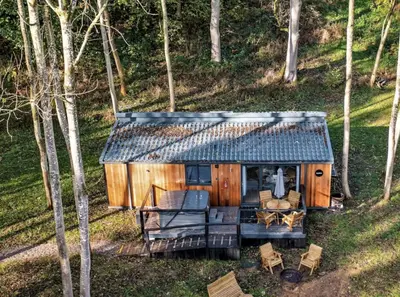 a small cabin with a couch and chairs in the woods at Riverside Cabins in Shrewsbury