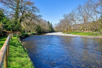 a river with a fence next to a field and trees at Finest Retreats - Felin Ship in Dolgellau