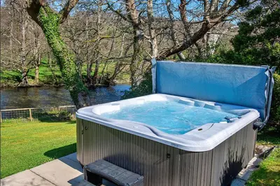 a jacuzzi tub sitting in a yard next to a river at Finest Retreats - Felin Ship in Dolgellau