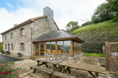 a conservatory with a wooden table in front of a building at 5 Bed in Aberystwyth oc-wan443 in Llanychaiarn