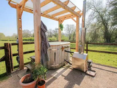 a wooden gazebo with a hot tub in a field at Balwen Shepherd's Hut in Montgomery